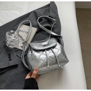 Side view of silver quilted mini backpack with metallic chain strap and drawstring closure