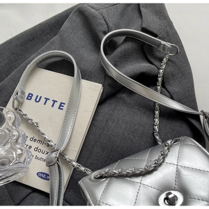 Detail of silver quilted cross body bag with chain strap on grey blazer fabric