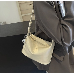 Detail of cream crossbody bag with crocodile pattern and silver ball charm on a model