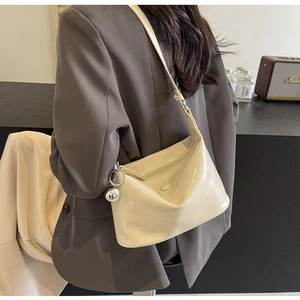 Detail view of cream crocodile texture hobo bag with silver ball pendant on suit shoulder