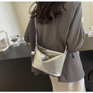 Silver textured crossbody bag with metallic sphere charm worn by model in minimalist cafe