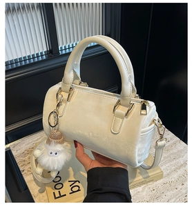 Detail of cream Boston bag with leather handles, gold hardware, and a plush monster charm