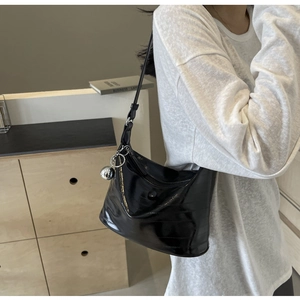 Detail of black glossy shoulder bag with a large silver spherical charm and pleated texture