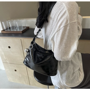 Close-up of black glossy patent leather shoulder bag with a silver sphere charm