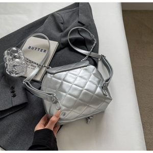 Close-up of metallic silver quilted handbag with adjustable chain strap on grey blazer