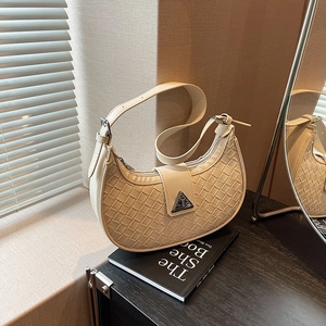 Chic cream woven crescent hobo bag with silver triangle buckle on a black book