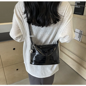 Detail of black glossy crossbody bag with horizontal texture and silver metal ball charm