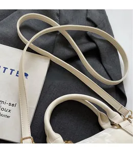 Close-up of adjustable long shoulder strap and golden metal buckles on cream handbag