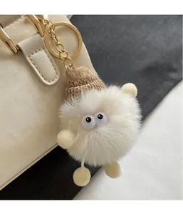 Cute plush monster charm with a brown knit hat and gold ring on an off-white handbag