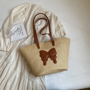Beige straw tote bag with brown leather bow detail and long straps on white fabric