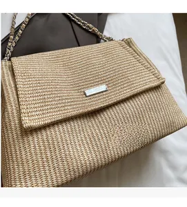 Detail of beige woven straw shoulder bag with chain strap and metallic logo plate