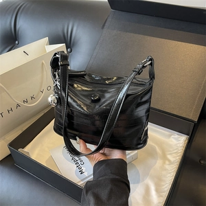 Detail of black glossy hobo bag with silver ball charm inside a gift box
