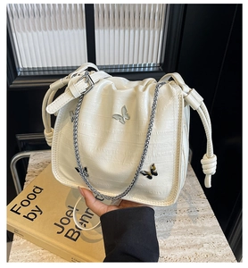 Close-up of cream-white bucket bag with embossed crocodile texture and silver butterfly charms