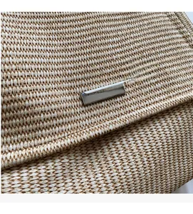 Close-up of woven straw texture and rectangular silver metal logo plaque on a shoulder bag