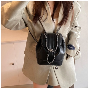 Detail of a black leather bucket backpack featuring a gold chain strap and turn-lock closure