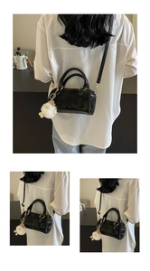 Detail of black Boston bag with gold hardware and white plush keychain accessory