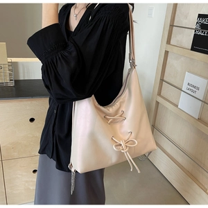 Close-up of minimalist beige tote bag featuring cross-strap bow and metal chain details