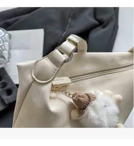 Detail of cream dumpling bag with metallic sheen, gold zipper and soft plush charm