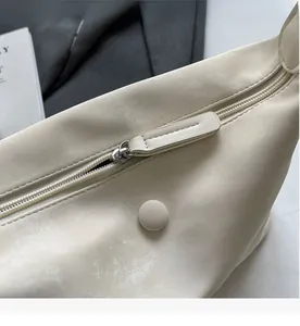 Close-up of smooth metal zipper and decorative button on beige minimalist crossbody bag