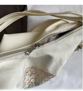 Close-up of smooth silver zipper and delicate embroidery on off-white crossbody bag