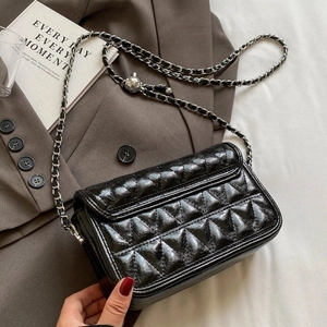 Quilted black leather chain shoulder bag with adjustable metal ball on a stylish suit background