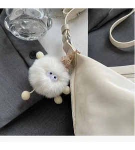 Detail of white furry monster charm with big eyes on a minimalist cream shoulder bag