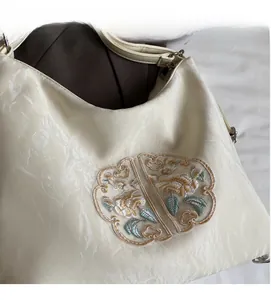 Detailed close-up of exquisite floral embroidery on a pleated beige shoulder bag