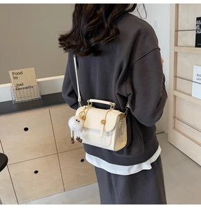 Detail of a minimalist cream crossbody bag with metal snap and a cute plush charm accessory