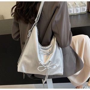Macro detail of metallic silver tote bag with lace-up bow and chain strap on shoulder