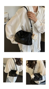 Detail of black glossy leather dumpling bag with white plush lamb pendant and metal buckle