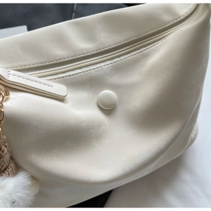 Detailed view of off-white PU leather bag texture with smooth zipper and plush charm
