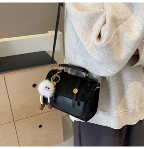 Detail of black PU leather handbag with gold buckle and cute plush doll charm