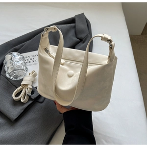 Detail of creamy white dumpling bag with wrinkled faux leather texture and round buckle