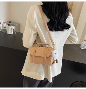 Detail of apricot crossbody bag with gold hardware and a cute white plush charm