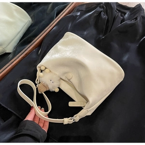 Close-up of cream dumpling bag with pearl finish, cute sheep charm, and black satin backdrop