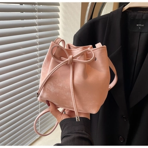 Détail du sac seau rose à cordon avec nœud et texture mate lisse porté par le mannequin