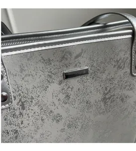 Detail showing silver textured tote bag surface with metal plaque and zip closure