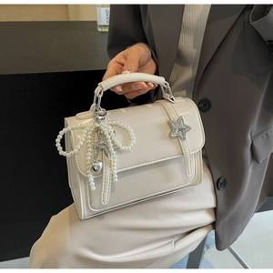 Détail d'un sac crème avec nœud en perles et étoile métallique tenu par un mannequin