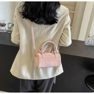 Rear view of a model wearing a pink suede Boston bag with a beige suit in a cafe