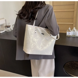 Detailed view of white glossy tote bag with silver crackle texture on grey blazer