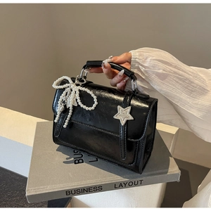 Détail du sac à main noir brillant avec nœud perlé et boucle en étoile argentée