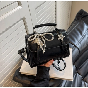 Détail d'un sac bandoulière noir avec boucles en étoile et nœud en perles blanches