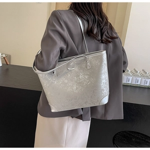 Detail of silver metallic tote bag featuring shimmering texture and a small metal logo plate