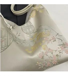 Close-up of silk embroidery on the beige shoulder bag with floral and bamboo patterns