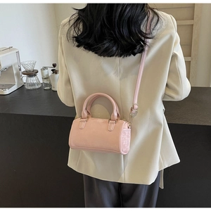 Detailed view of pink Boston bag with gold hardware held by model in cream blazer