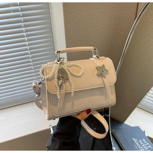 Détail d'un sac à main blanc crème avec boucle en métal étoilée et pendentif noeud perlé