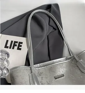 Detailed view of silver metallic tote bag with sleek long shoulder straps and metal logo
