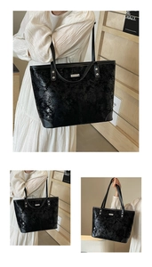 Detail of black patent leather tote bag with cracked texture and silver metal plaque