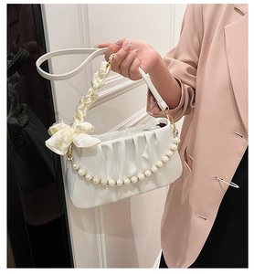Close-up of white pleated bag featuring pearl chain strap and silk ribbon handle detail