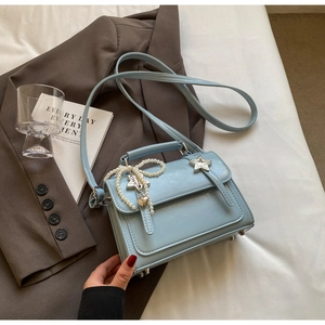 Détail du sac bandoulière bleu clair avec clous étoilés et breloque nœud en perles